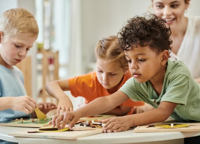african american kid playing with didactic material near children and teacher in montessori school