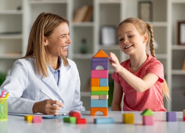 Child Development Specialist Looking At Little Girl Playing With Colorful Wooden Bricks